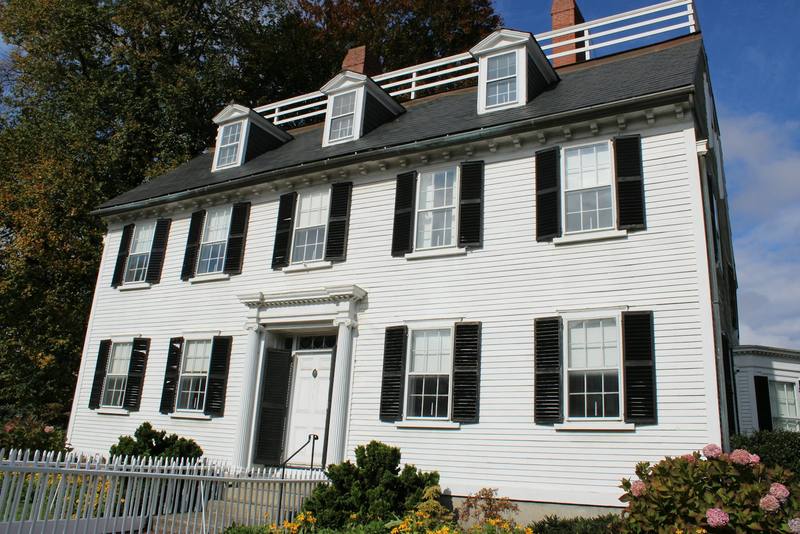 A white New England colonial with black shutters seen from the street. Reference photograph.