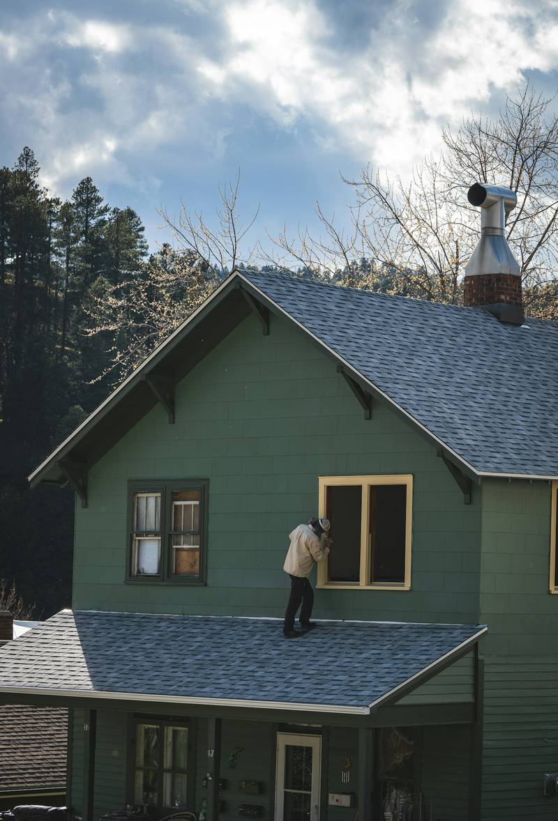 A painter working at an upstairs window of a green house. Reference photograph.